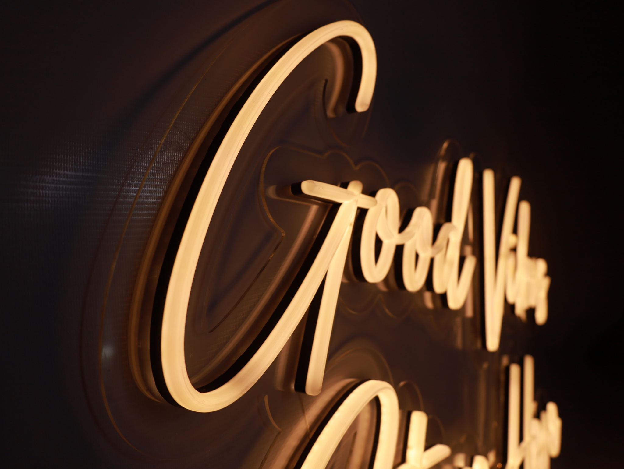 ป้ายนีออนตัวเขียนคำว่า Good Vibes โทนแสงอุ่นถ่ายระยะใกล้ด้านข้าง