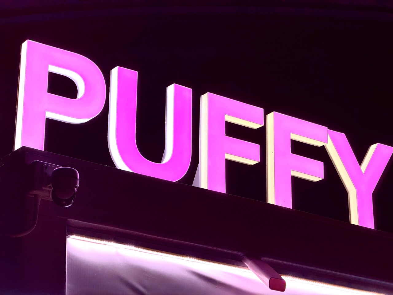 ป้ายไฟคำว่า PUFFY สีชมพูเรืองแสงติดบนผนัง
