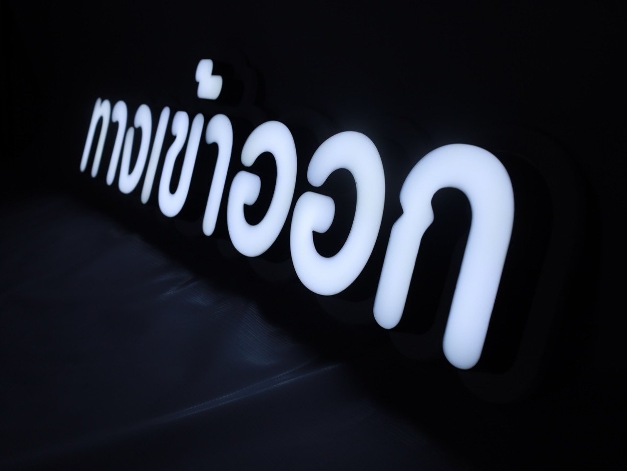 ป้ายไฟภาษาไทยสีขาวบนพื้นหลังสีดำ ถ่ายมุมเฉียง