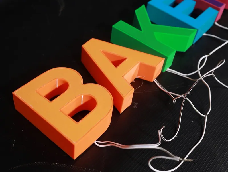 ตัวอักษรสามมิติหลายสี B A K E วางเรียงพร้อมสายไฟ