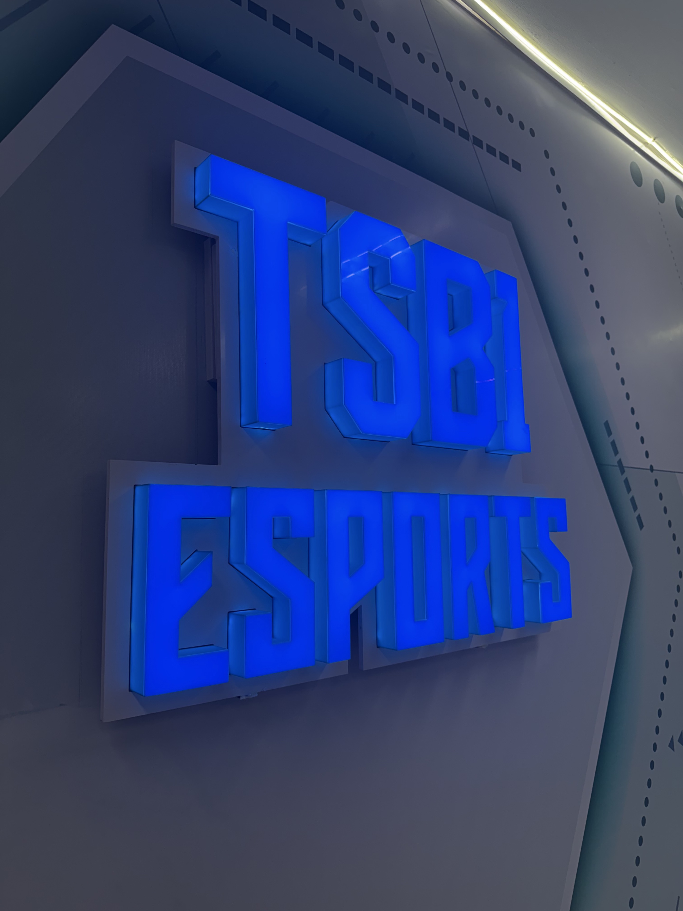 ป้ายไฟคำว่า TSBI ESPORTS สีฟ้าน้ำเงินติดบนผนัง